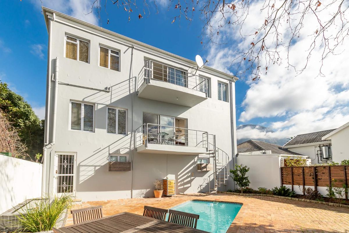 Rear exterior view of a multi-story townhouse featuring a private swimming pool, brick-paved patio area, and external balconies with a spiral staircase.