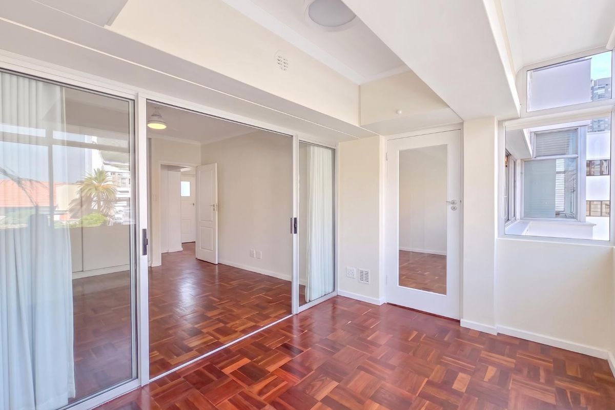 Bright and spacious living area featuring polished parquet flooring, large sliding glass doors, and mirrored built-in storage, offering a clean and versatile layout.