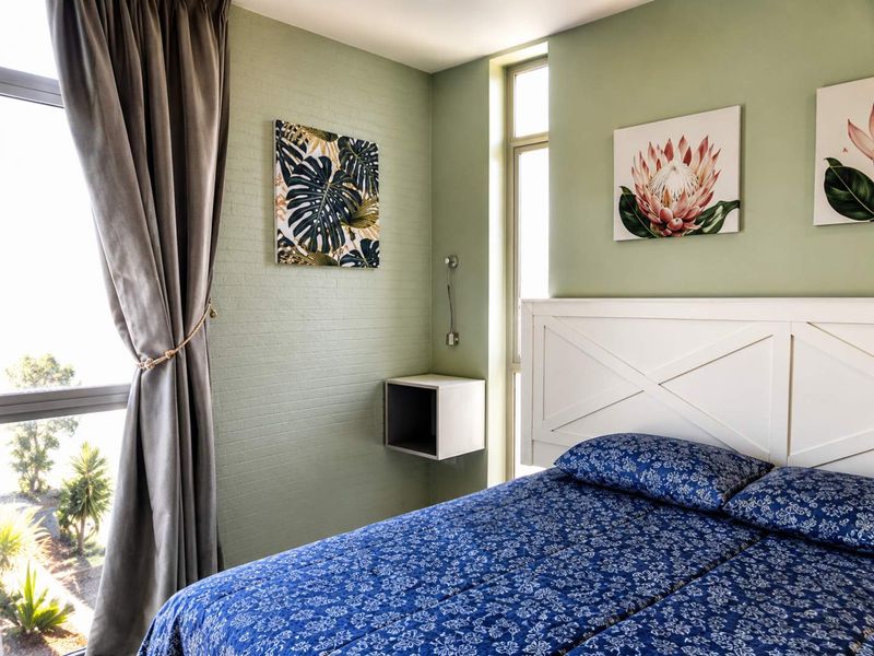 A well-lit bedroom featuring a large window, textured green accent wall, and a convenient built-in wall-mounted bedside shelf.