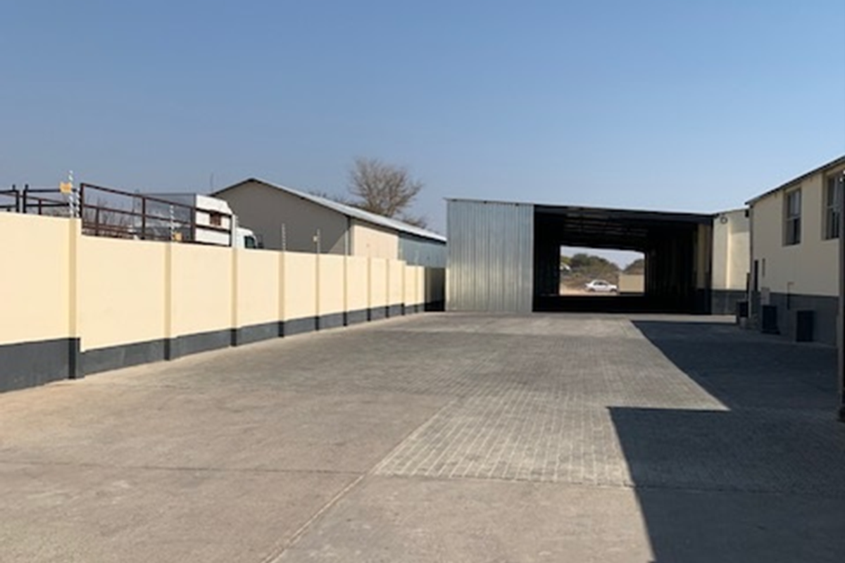 Spacious industrial yard featuring concrete paving, perimeter boundary wall with electric fencing, and a large open-sided warehouse structure.