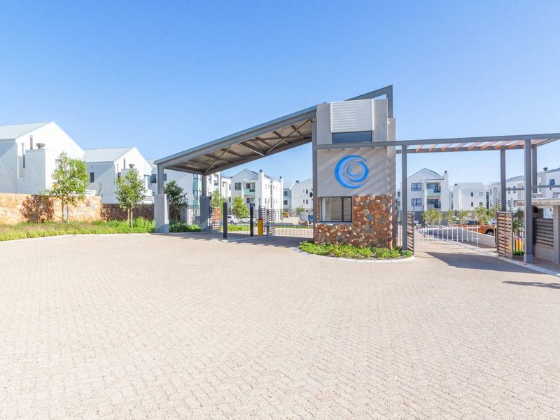 Modern security gatehouse entrance to the apartment complex featuring stone cladding and a paved driveway.