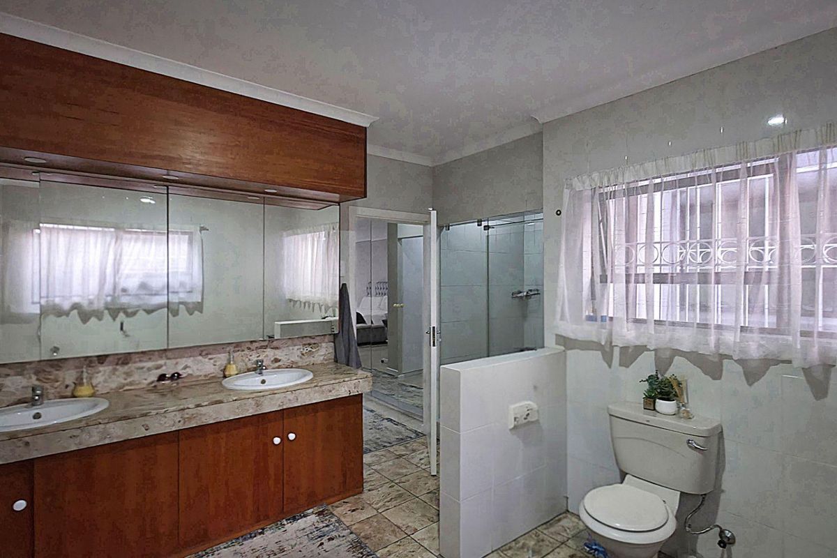 A functional bathroom featuring a double vanity with stone countertop, built-in wooden cabinetry, a glass-enclosed shower, and tiled flooring.