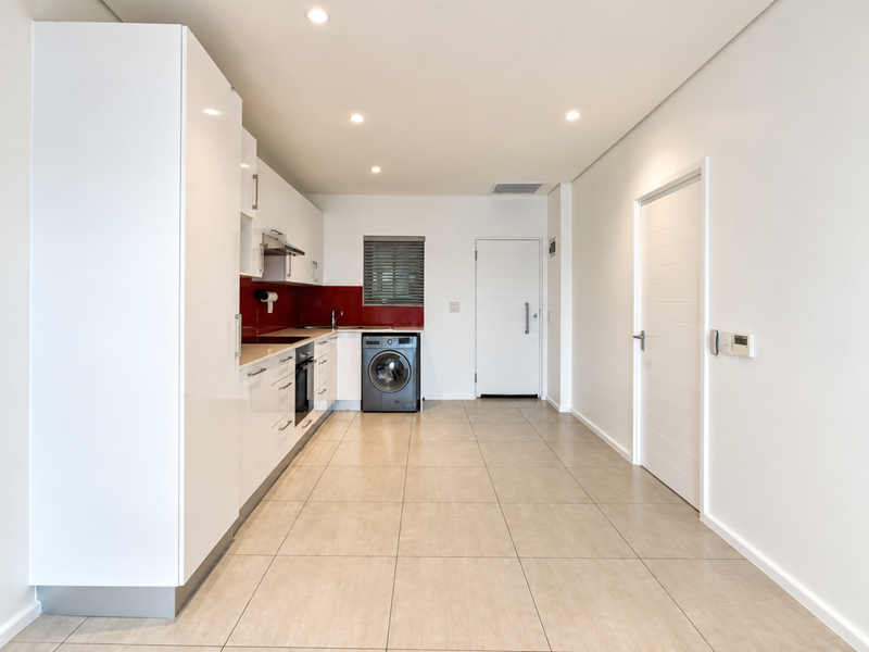 Modern kitchen featuring sleek white cabinetry, integrated appliances, a bold red splashback, and neutral floor tiles in a clean, open-plan layout.