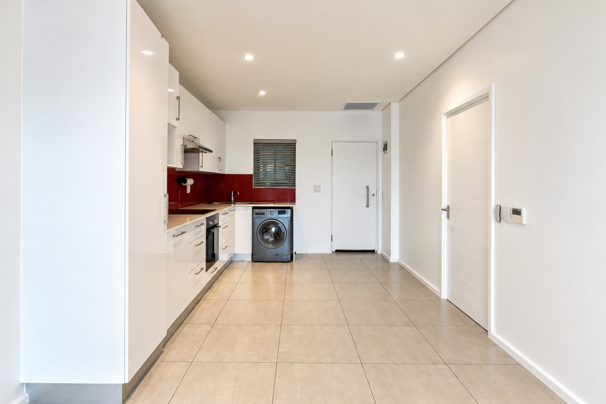 Modern kitchen featuring sleek white cabinetry, integrated appliances, a bold red splashback, and neutral floor tiles in a clean, open-plan layout.