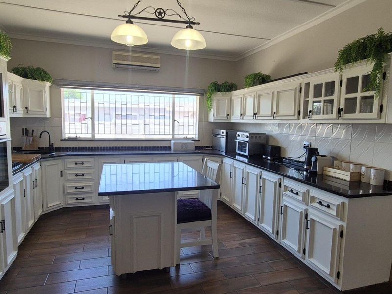 Spacious kitchen featuring white cabinetry, dark granite countertops, a central island, built-in oven, and tiled flooring with ample natural light.