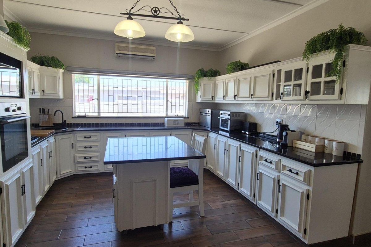 Spacious kitchen featuring white cabinetry, dark granite countertops, a central island, built-in oven, and tiled flooring with ample natural light.