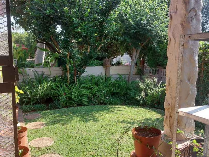 A covered patio area overlooking a private garden with a lawn, mature trees, and a stone-clad structural pillar.
