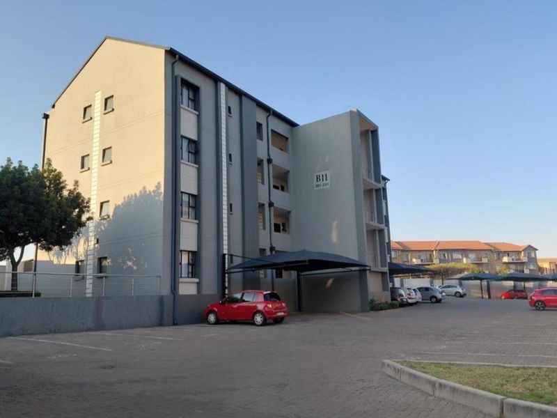 Exterior view of a multi-story apartment building featuring a paved parking area and covered carports.