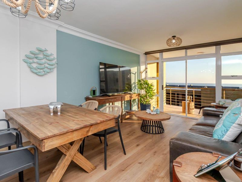 Bright open-plan living area featuring laminate flooring, crown molding, and large sliding glass doors leading to a balcony with ocean views.