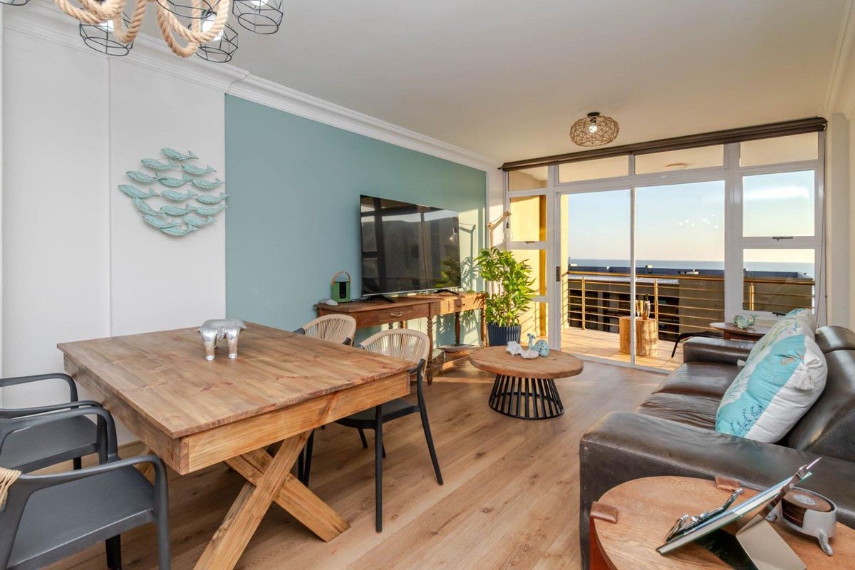 Bright open-plan living area featuring laminate flooring, crown molding, and large sliding glass doors leading to a balcony with ocean views.