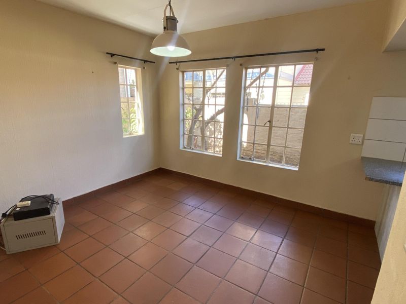 An empty living area featuring terracotta tiled flooring, natural light from multi-pane windows, and a neutral wall finish, ready for personalization.