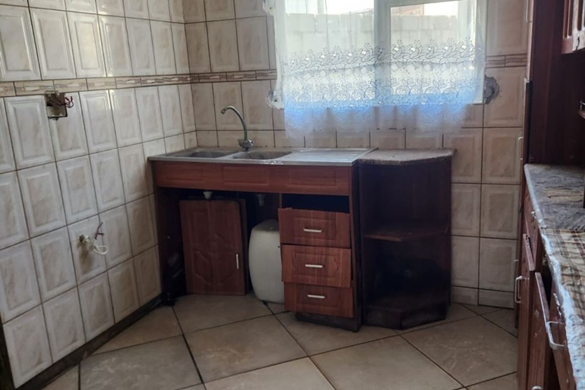 A dated kitchen featuring tiled walls and flooring, a single sink unit, and built-in cabinetry, currently in need of renovation and repair.