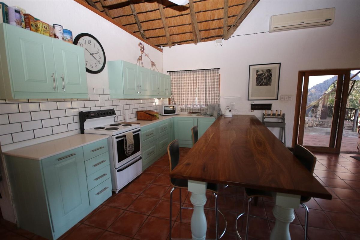 A kitchen featuring light green cabinetry, subway tile backsplash, a wooden breakfast bar, and a traditional thatched roof ceiling.