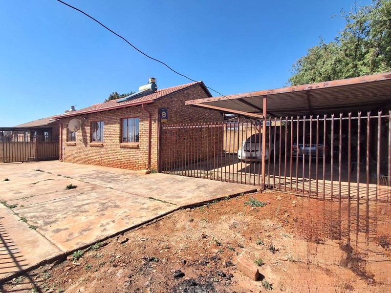 Front exterior view of a face brick house featuring a tiled roof, solar geyser, and a covered carport with steel security fencing.