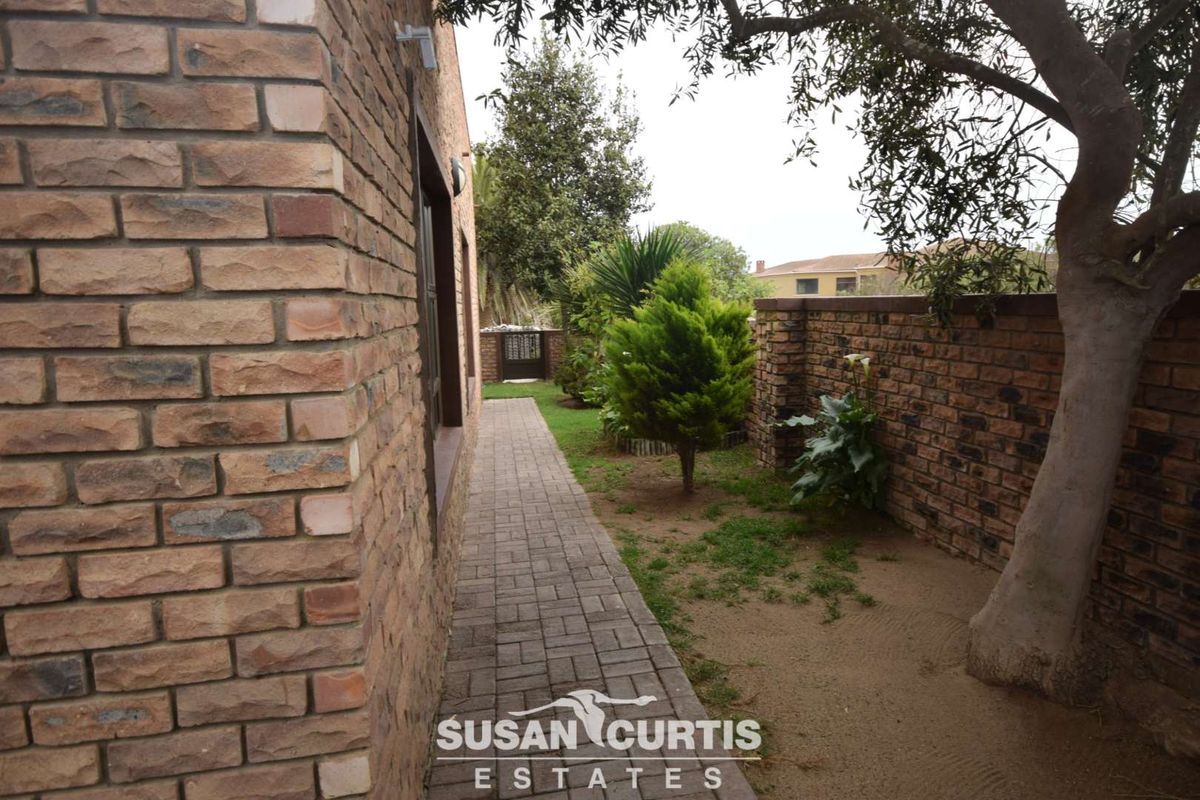A side garden pathway featuring brick paving, a brick boundary wall, and established trees along the side of the house.