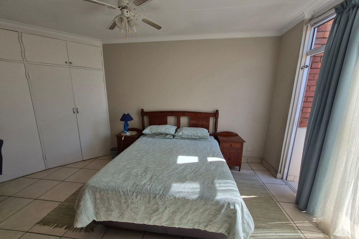 A bedroom featuring built-in cupboards, tiled flooring, and a ceiling fan, with direct access to an outdoor area through a glass door.