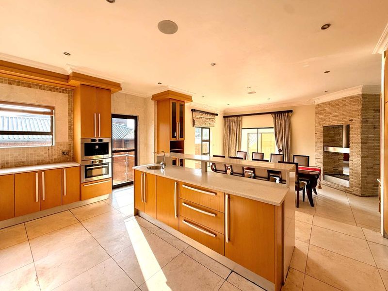 Spacious open-plan kitchen and dining area featuring warm wood cabinetry, stone countertops, a central island, and a prominent stone fireplace.