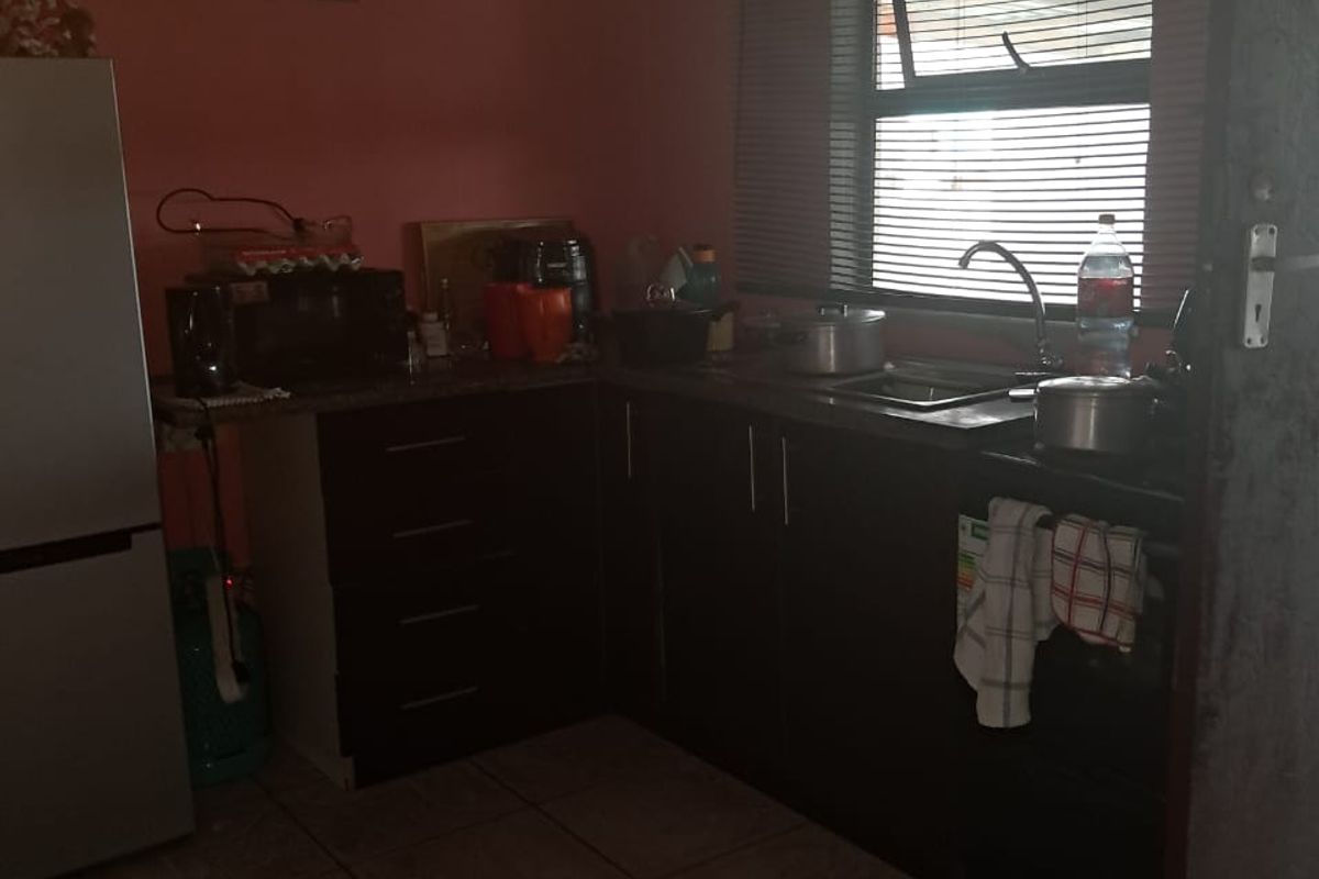 A compact kitchen featuring dark built-in cabinetry, a stainless steel sink, and tiled flooring, requiring some cosmetic updates to improve its overall appeal.