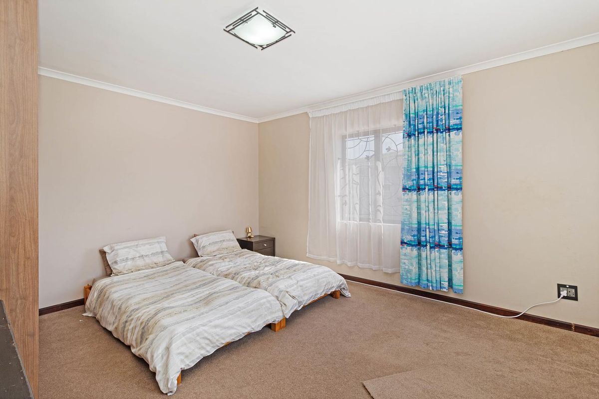 A spacious bedroom featuring neutral wall tones, carpeted flooring, a built-in wardrobe, and a window fitted with security bars.
