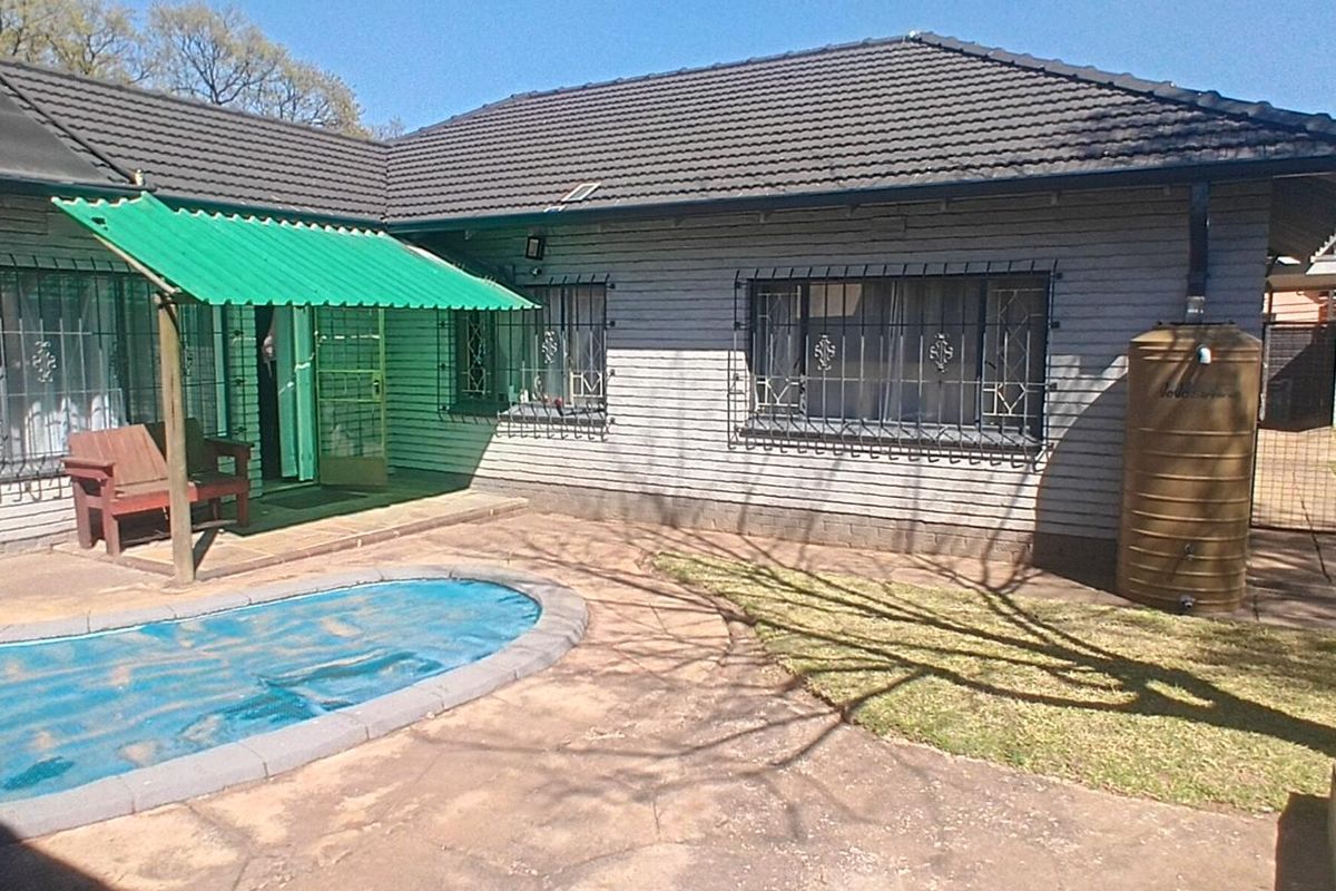 Rear exterior view of the house featuring a swimming pool, paved patio area, green awning, and a water tank.