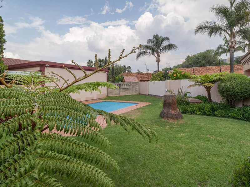 A private backyard featuring a swimming pool with brick coping, surrounded by a well-maintained lawn and secure perimeter walling with electric fencing.