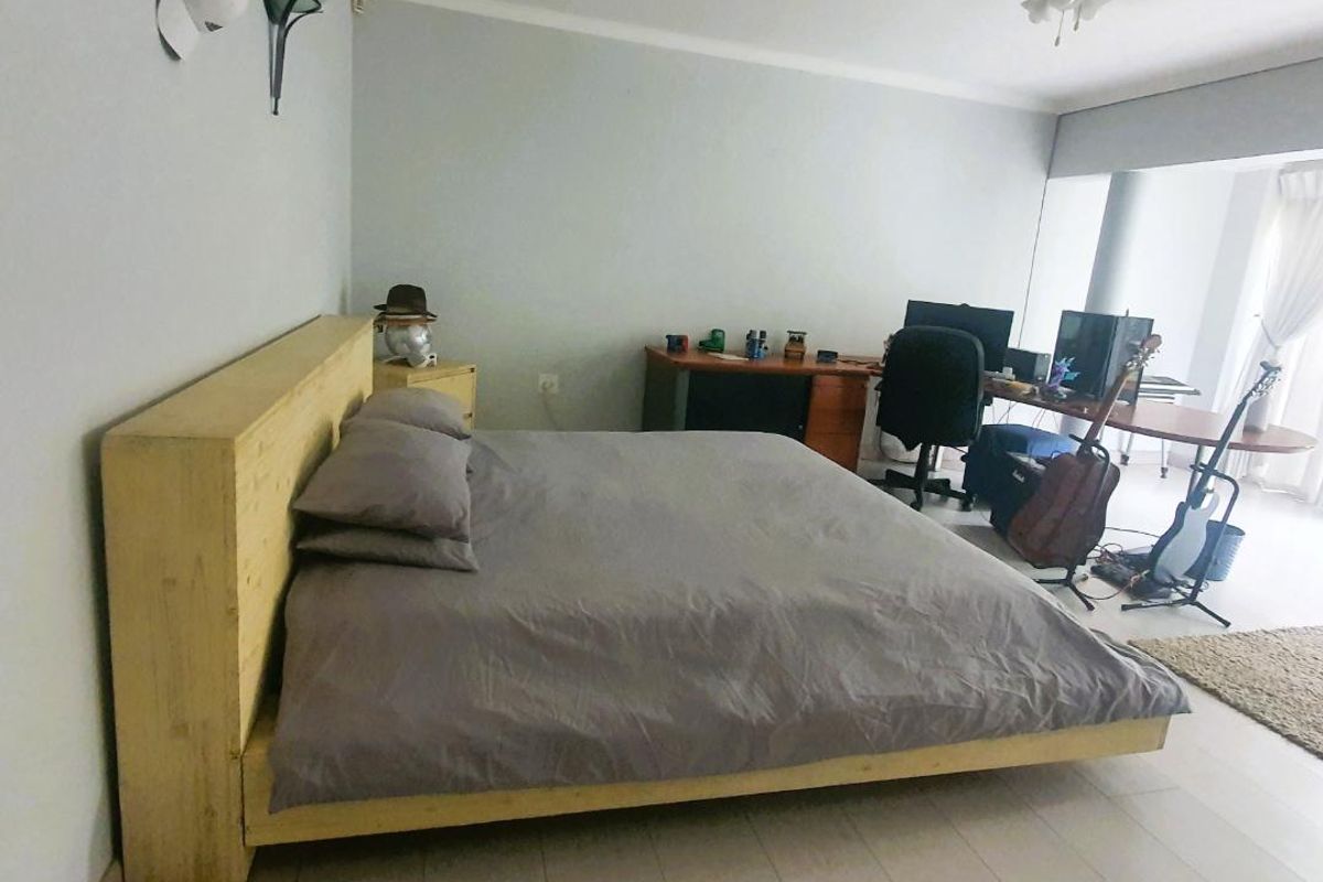 A spacious bedroom featuring tiled flooring, a ceiling fan, and neutral wall finishes, offering a versatile layout for sleeping and workspace areas.