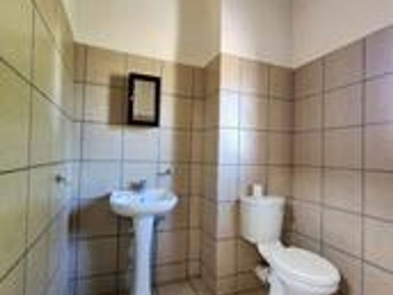 A functional bathroom featuring a pedestal washbasin, toilet, and full-height wall tiling with exposed ceiling beams.