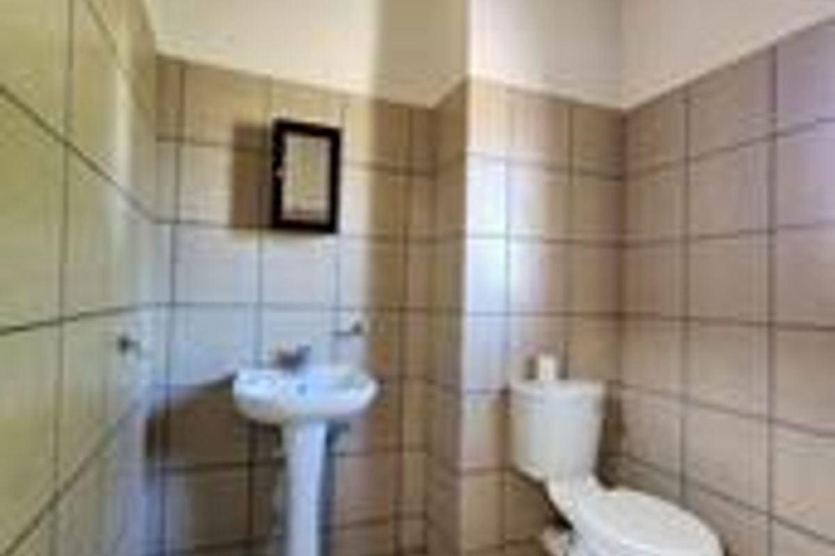 A functional bathroom featuring a pedestal washbasin, toilet, and full-height wall tiling with exposed ceiling beams.