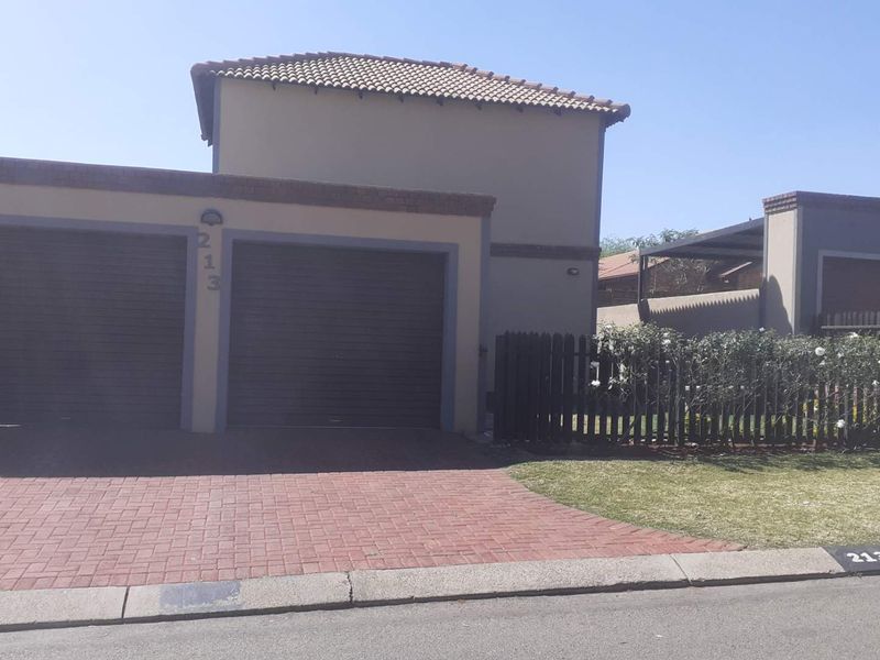 Front exterior view of a cluster home featuring a double garage, paved driveway, and a small front garden with a picket fence.
