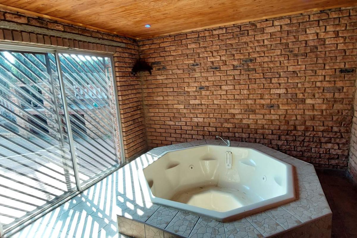 Indoor spa room featuring a built-in corner jacuzzi tub, exposed brick walls, timber-clad ceiling, and large sliding glass doors leading to the exterior.