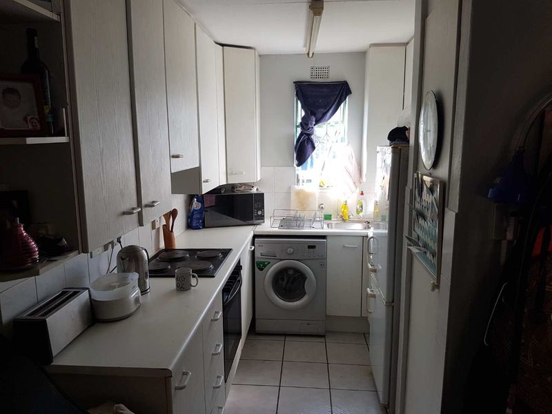 A compact galley-style kitchen featuring white cabinetry, an integrated electric hob and oven, tiled flooring, and a dedicated space for a washing machine.