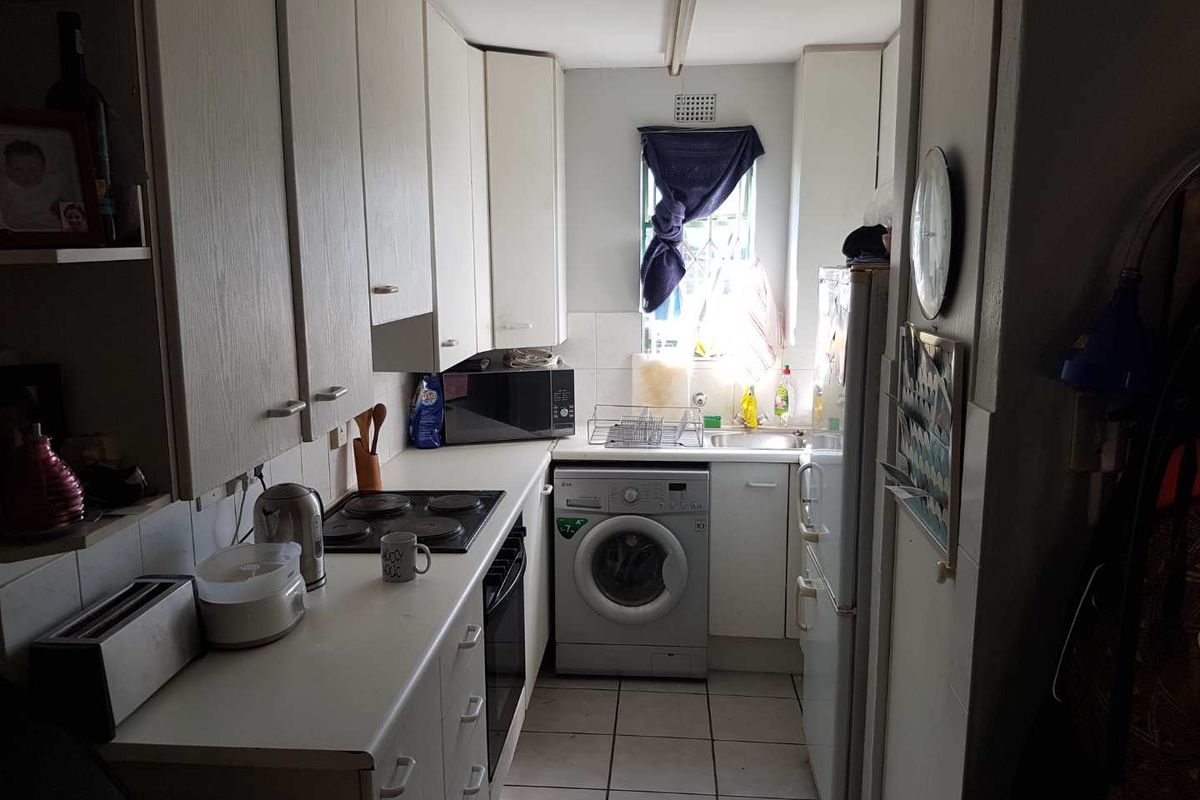 A compact galley-style kitchen featuring white cabinetry, an integrated electric hob and oven, tiled flooring, and a dedicated space for a washing machine.