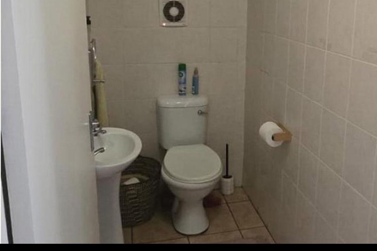 A compact guest bathroom featuring a pedestal basin, a standard toilet, and tiled walls with an integrated extractor fan.