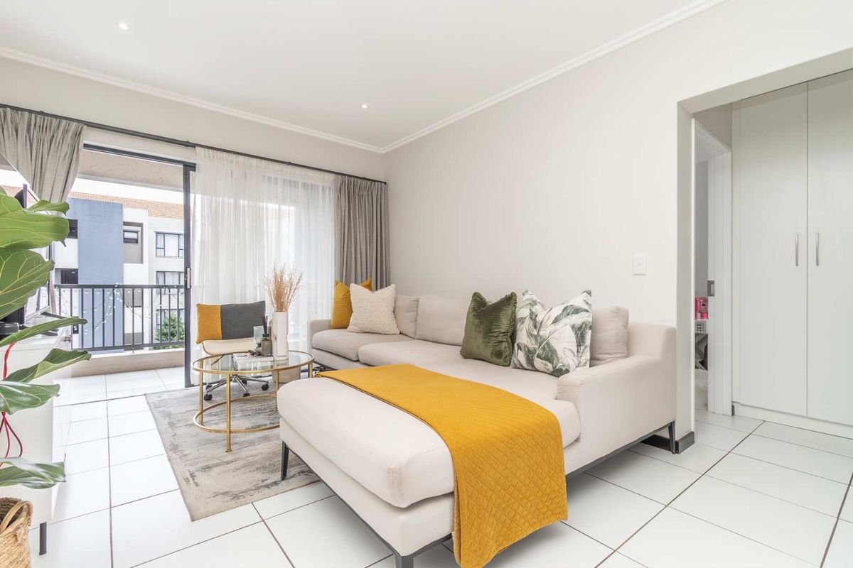 Bright living area featuring large sliding glass doors leading to a private balcony, tiled flooring, and built-in storage cupboards in the adjacent hallway.