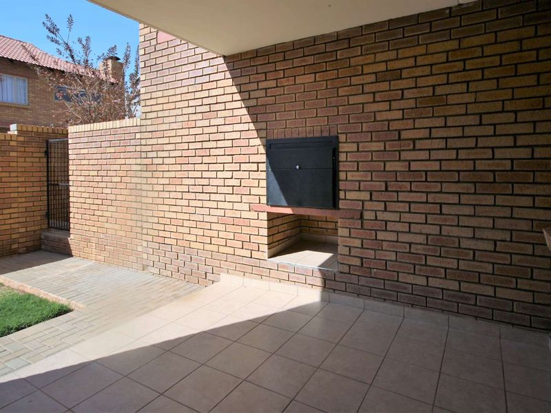 Covered patio area featuring a built-in braai, tiled flooring, and direct access to a small paved garden space.