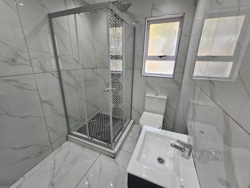 A modern bathroom featuring marble-look wall and floor tiles, a glass shower enclosure with decorative accent tiling, a vanity basin, and a toilet.
