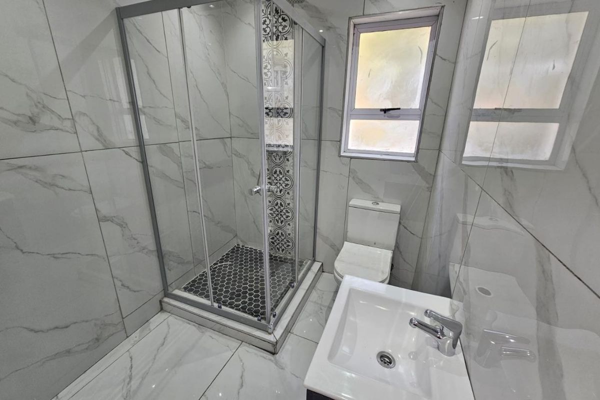A modern bathroom featuring marble-look wall and floor tiles, a glass shower enclosure with decorative accent tiling, a vanity basin, and a toilet.