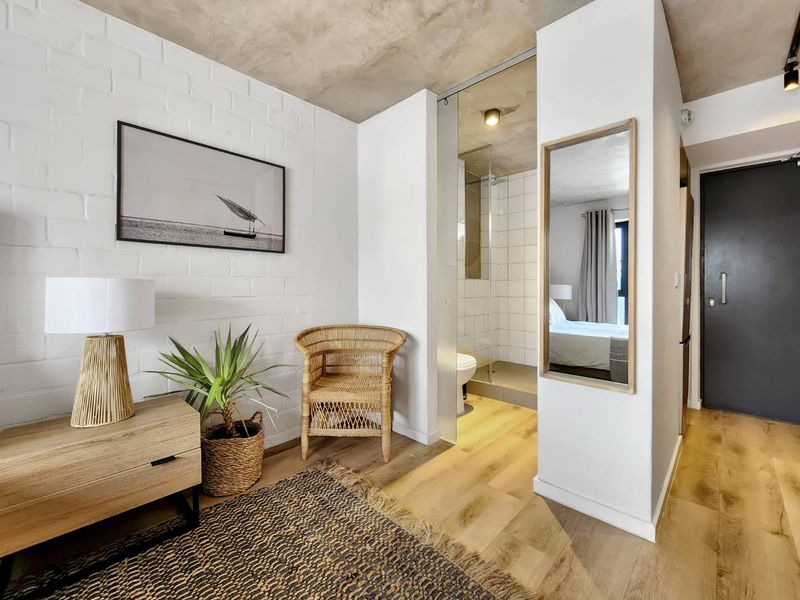 Modern bedroom featuring an exposed concrete ceiling, painted brick wall, laminate flooring, and an integrated glass-enclosed shower area.