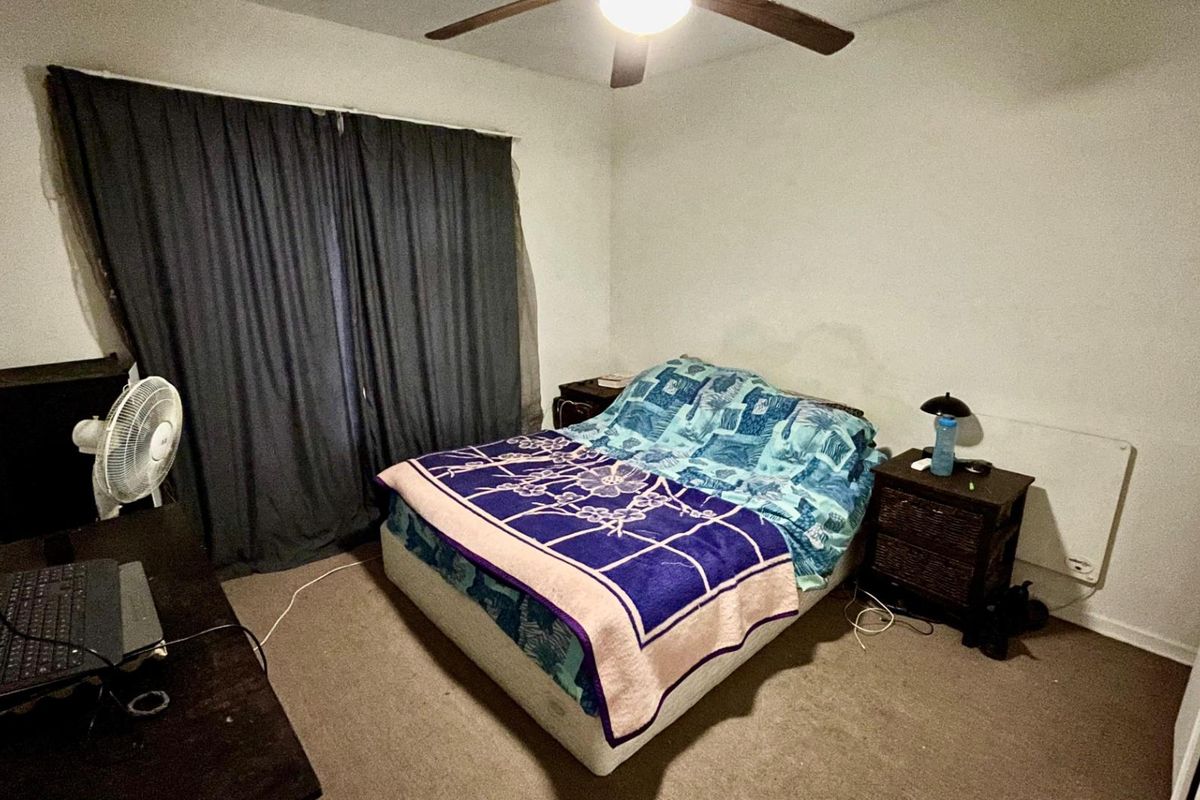 A standard bedroom featuring a ceiling fan, wall-mounted heater, and carpeted flooring.