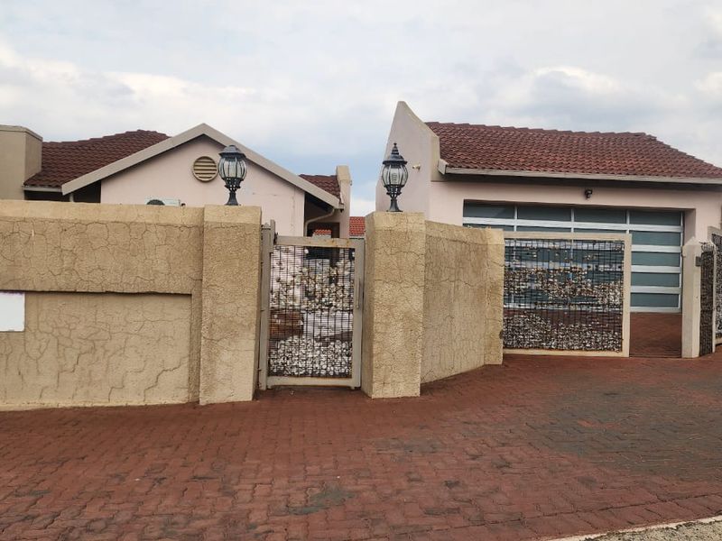 Front exterior view of the property featuring a paved driveway, boundary wall with pedestrian gate, and a modern garage door.