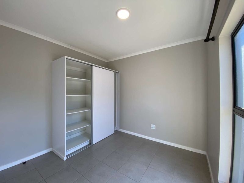 A clean, neutral-toned bedroom featuring tiled flooring, a built-in sliding door wardrobe, and a modern recessed ceiling light.