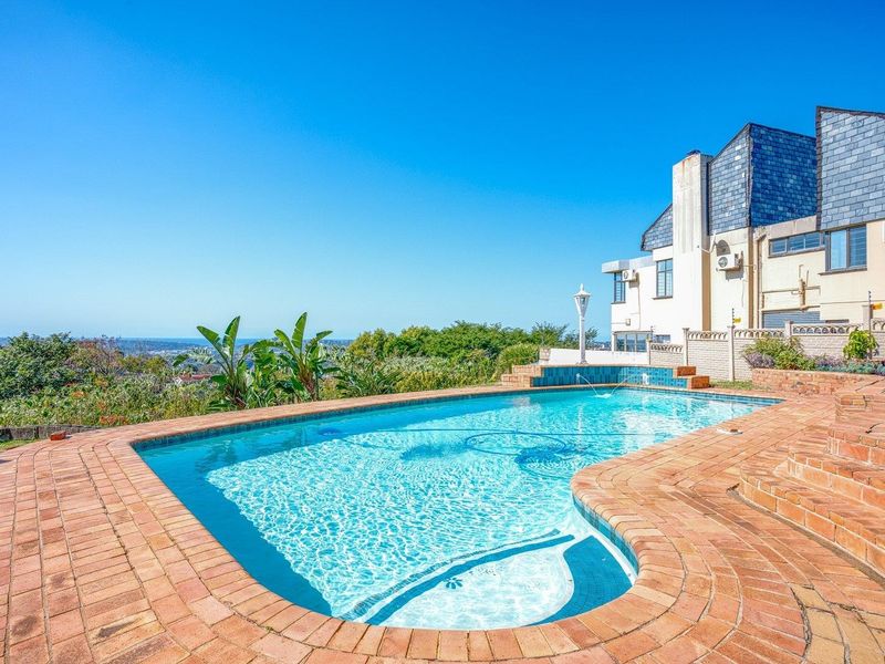 A well-maintained swimming pool area featuring brick paving, a tiled water feature, and expansive views, set against the rear elevation of the property.