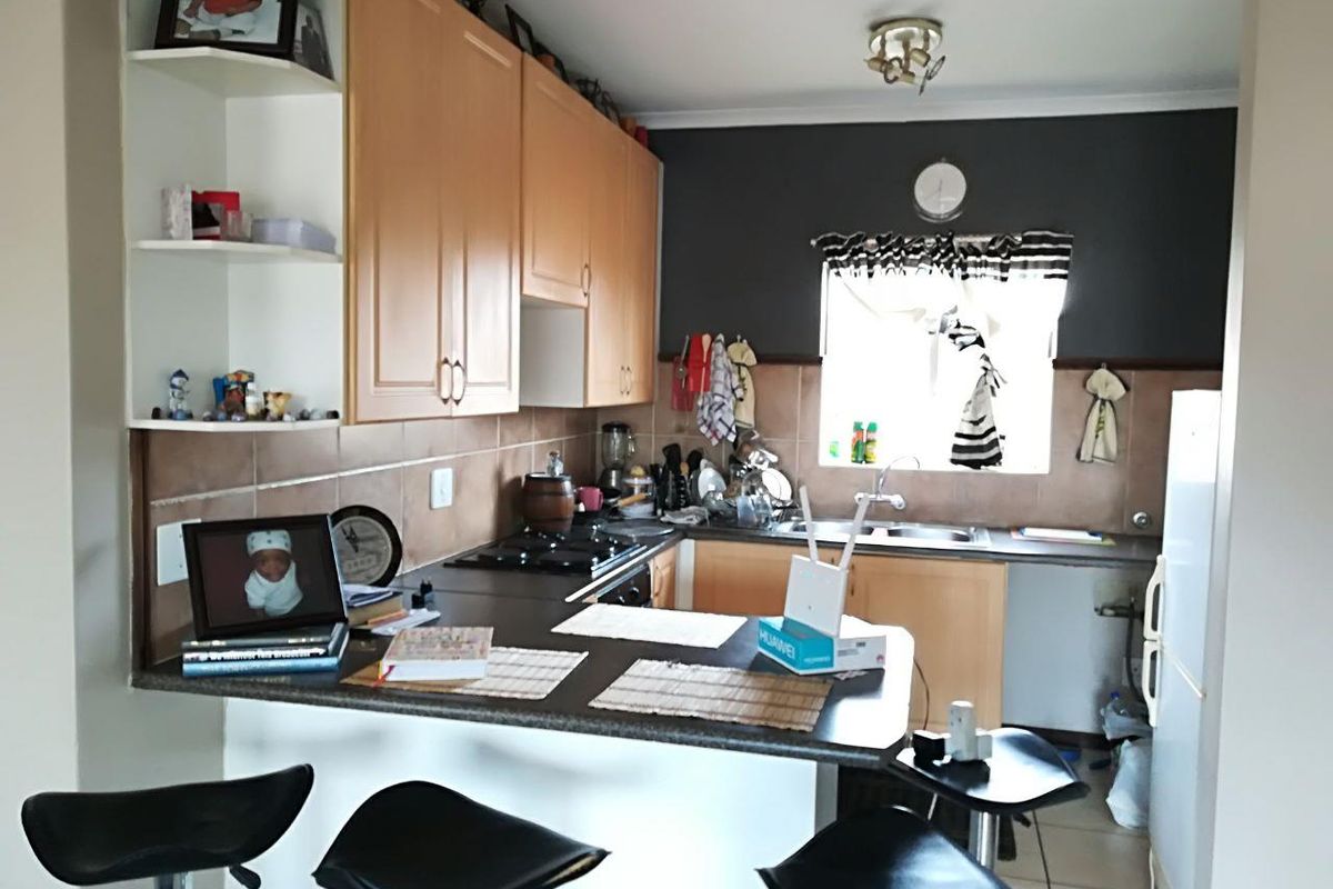 A functional kitchen featuring wooden cabinetry, a gas hob, tiled backsplash, and a breakfast bar counter, offering a practical layout for daily meal preparation.