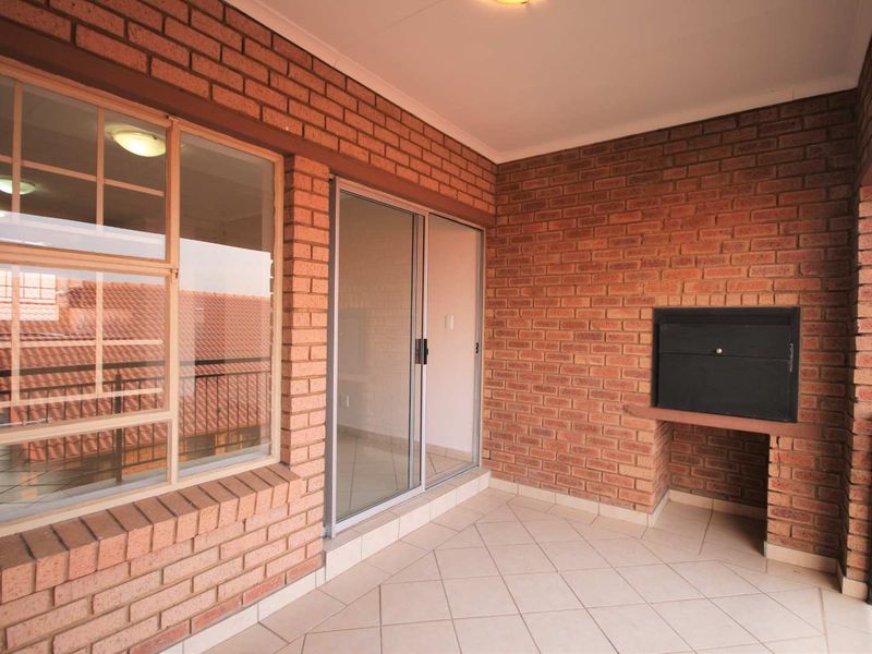 A spacious covered balcony featuring exposed brick walls, tiled flooring, and a built-in braai, offering a functional outdoor entertainment area.
