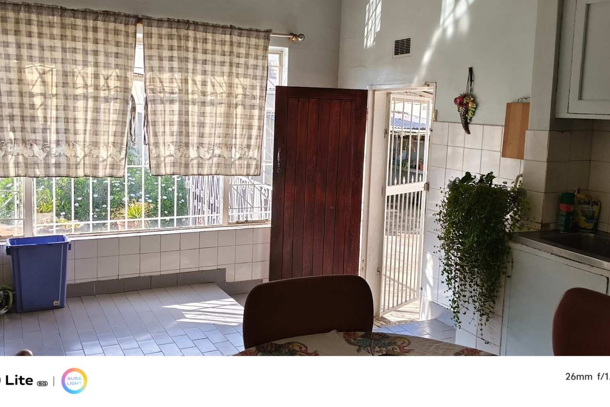 A functional kitchen area featuring tiled flooring, built-in cabinetry, a stainless steel sink, and direct access to the exterior through a security gate.