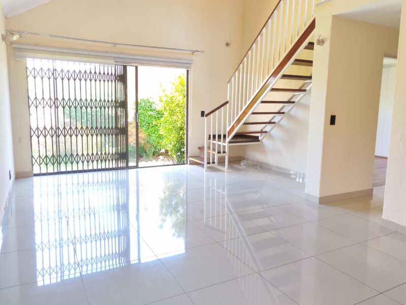 Spacious open-plan living area featuring polished tile flooring, a modern staircase with wooden treads, and large sliding doors leading to the garden.