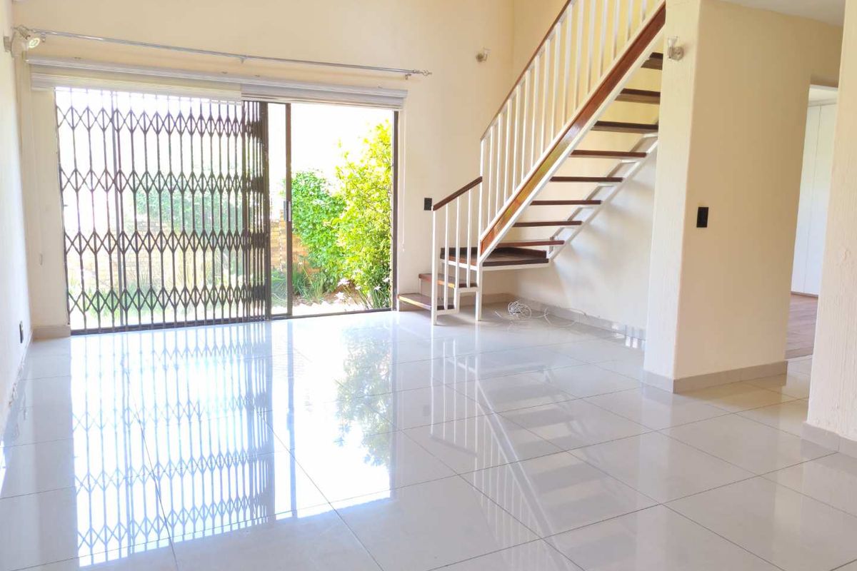 Spacious open-plan living area featuring polished tile flooring, a modern staircase with wooden treads, and large sliding doors leading to the garden.