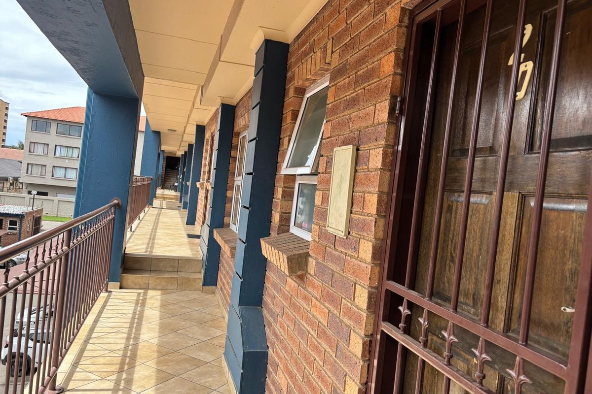 An exterior walkway corridor featuring tiled flooring, brick facade, and metal security gates providing access to apartment units.