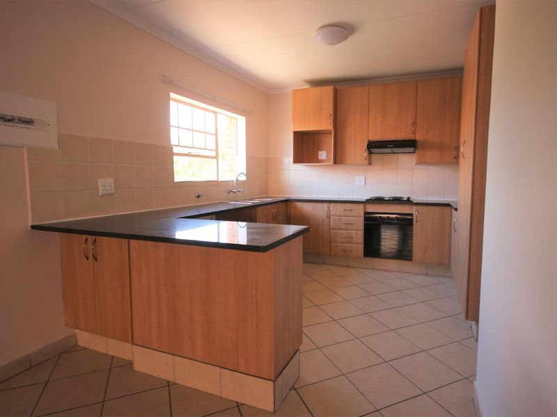 A functional, empty kitchen featuring wood-finish cabinetry, dark laminate countertops, built-in oven, hob, extractor fan, and tiled flooring.
