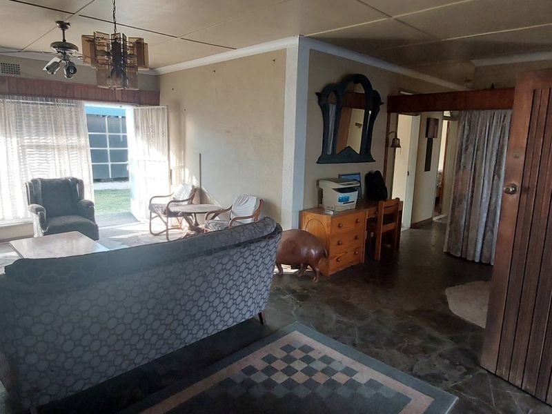 Spacious living room featuring natural stone flooring, a ceiling fan, and a fireplace, offering a dated interior ready for modernization and renovation.